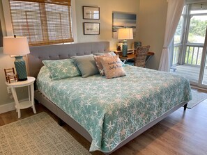 A bedroom with a large bed, a nightstand, a lamp, and a view of the outdoors.