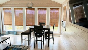 A modern dining area with a wooden table and chairs, large windows with blinds, and a view of the outdoors.