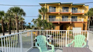 A multi-story building with balconies, a parking area, and a view of the ocean.