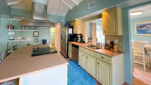 A kitchen with a central island, a stainless steel range hood, and a refrigerator. There is a window with a view of the outdoors.