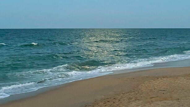 A beach with a clear sky and the sun visible above the horizon.