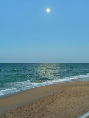 Une plage avec un ciel dégagé et le soleil visible au-dessus de l’horizon.