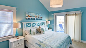 A bedroom with a bed, nightstands, a lamp, and a window with blinds. - Sea No Evil: Dog friendly, family friendly, decks, close to the beach. (Ocracoke)