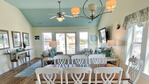 A dining area with a wooden table and white chairs, a ceiling fan, and a view of the outside. - Sea No Evil: Dog friendly, family friendly, decks, close to the beach. (Ocracoke)
