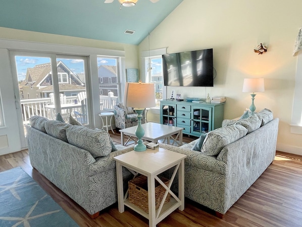Un salon doté d’une grande fenêtre, d’un téléviseur à écran plat, d’un meuble de couleur turquoise et de canapés à motifs.