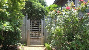 Een houten poort met een metalen raster, omringd door weelderige begroeiing en bloeiende planten.