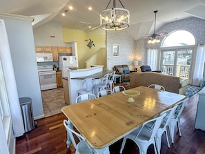 A spacious kitchen with modern appliances, a dining area with a wooden table and white chairs, and a living area with a sofa and a large window.