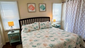 A bedroom with a bed, two nightstands, a lamp, a rug, and two framed pictures on the wall. - Mermaid Manor: Contemporary spacious home, decks and screened porches (Ocracoke)