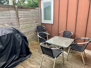 Un patio con una mesa, cuatro sillas, una parrilla cubierta y una valla de madera.