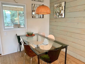 Un área de comedor moderna con una mesa de vidrio, sillas marrones y una lámpara colgante de fibras naturales.