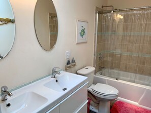 Baño con lavamanos doble, inodoro y ducha con cerramiento de vidrio.