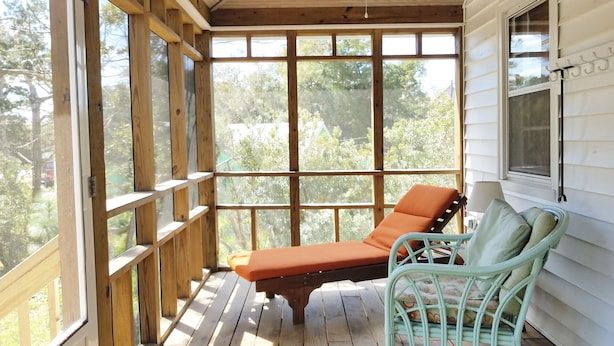 Eine überdachte Veranda mit Holzbalkonen, einem Deckenventilator und einer Sitzecke mit gepolstertem Sitz und einem Korbstuhl.