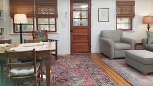 Ein gemütliches Wohnzimmer mit Holzboden, einem gemusterten Teppich, einem Esstisch mit Stühlen, einer Couch und einer Tür mit Fenster.