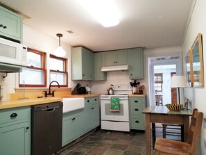 Kitchen area with dishwasher, sink, and stove, featuring a wooden table and chair.