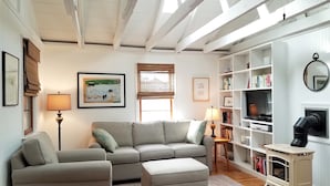 Ein Wohnzimmer mit Sofa, Hocker und Bücherregal.