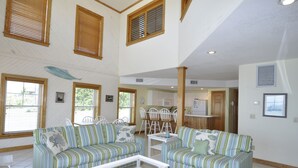 A spacious living area with two striped sofas, a white coffee table, and a dining table with chairs.