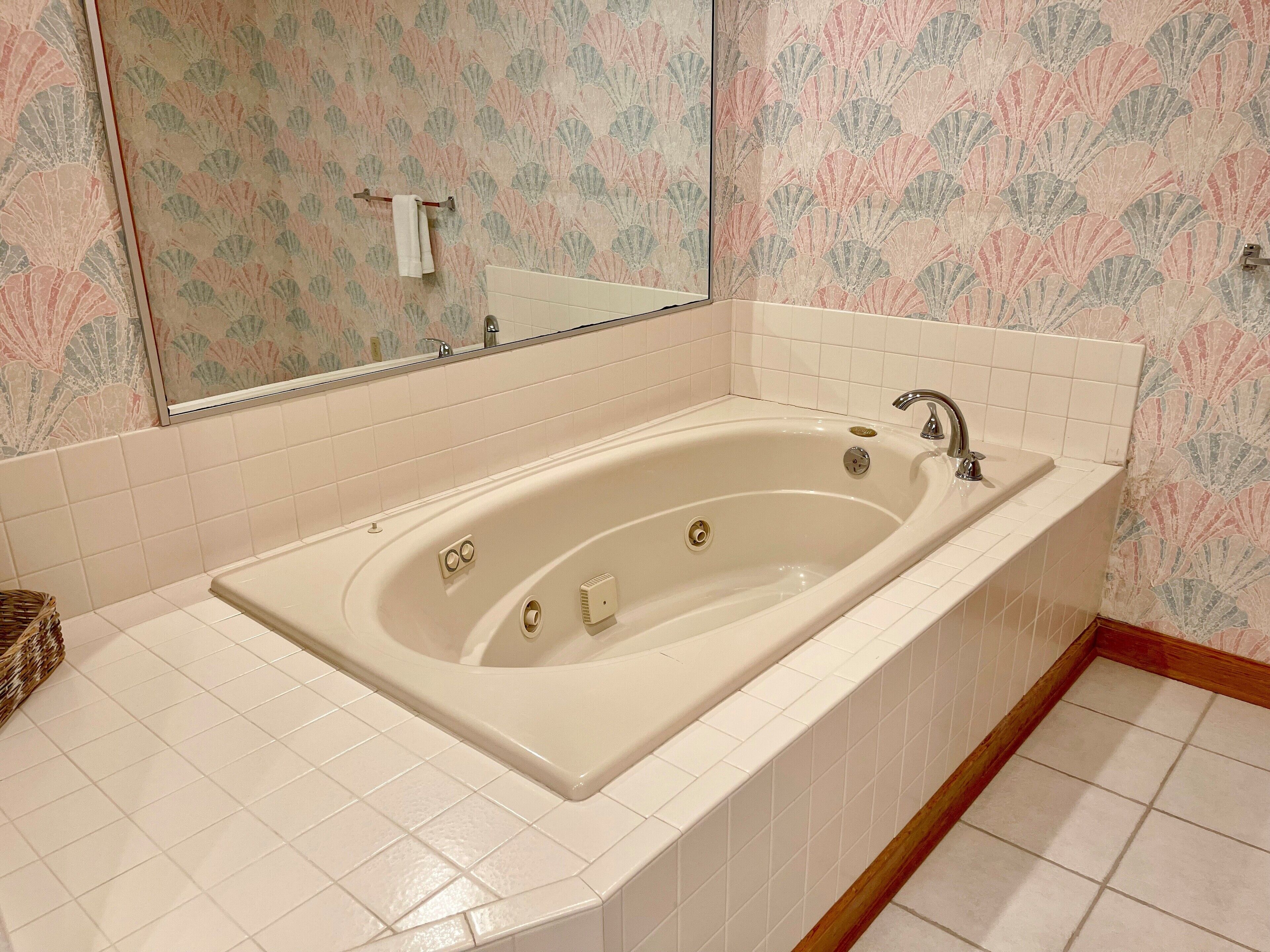 Un baño con bañera independiente, paredes de azulejos blancos y un espejo decorativo.