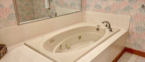 Un baño con bañera independiente, paredes de azulejos blancos y un espejo decorativo.