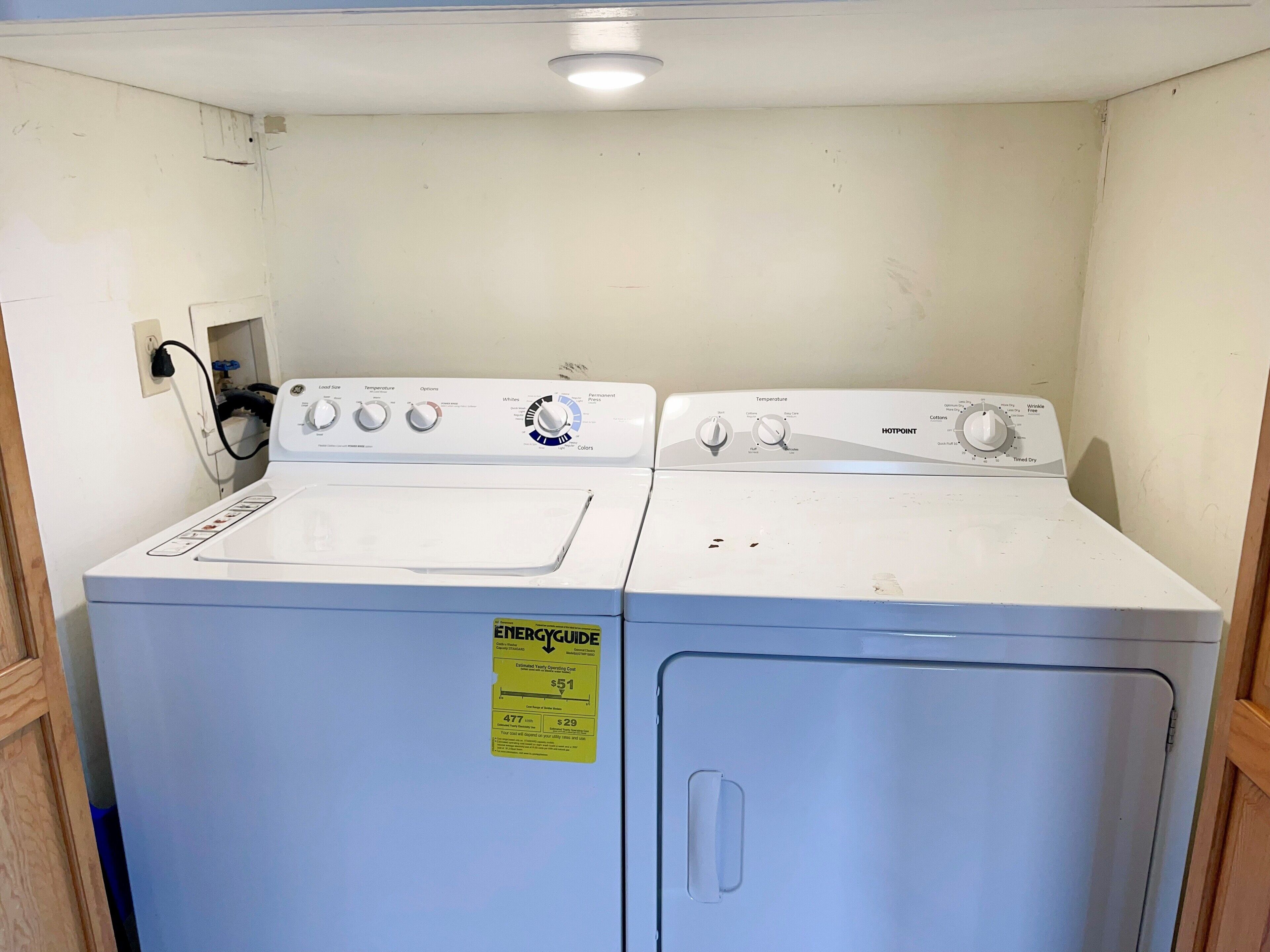 A laundry room with two stacked front-loading washing machines, a visible ENERGY GUIDE sticker, and a power outlet on the wall.