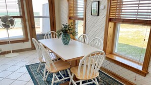 A dining area with a white table, six white chairs, a blue patterned rug, and a vase with flowers.