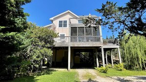 A two-story house with a balcony, surrounded by trees and a grassy yard. - Nicely Secluded Home, Short Stays Allowed (Ocracoke)