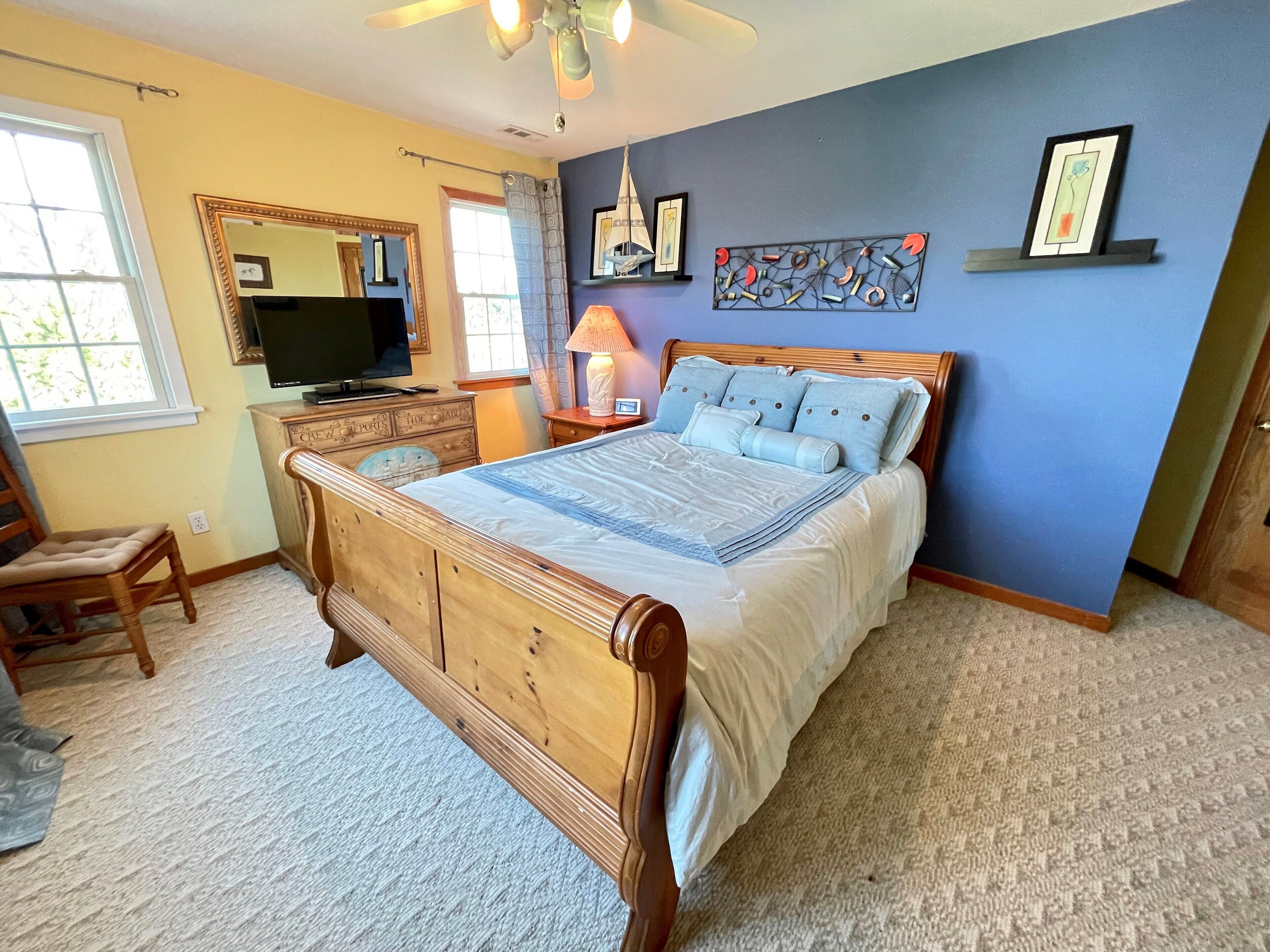 Quarto com cama de madeira, penteadeira, televisão e janela com cortinas.