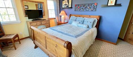 Quarto com cama de madeira, penteadeira, televisão e janela com cortinas.