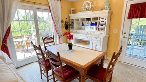 A dining area with a wooden table and chairs, a white cabinet with drawers, and a view of the outdoors through a glass door. - Nicely Secluded Home, Short Stays Allowed (Ocracoke)