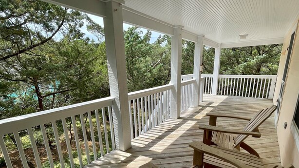 A wooden deck with white railings, two wooden chairs, and a view of trees. - Jetts House:  Dog friendly home in private location (Ocracoke)
