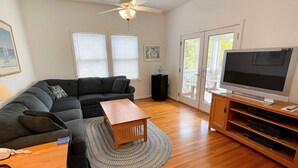 A living room with a sectional sofa, a wooden coffee table, a TV on a wooden stand, and a ceiling fan. - Jetts House:  Dog friendly home in private location (Ocracoke)