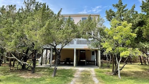 A two-story building with a covered porch and a staircase leading to the entrance. - Jetts House:  Dog friendly home in private location (Ocracoke)