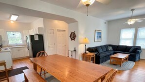 A spacious living room with a wooden dining table, a dark-colored sofa, and a small wooden coffee table. - Jetts House:  Dog friendly home in private location (Ocracoke)