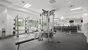 Un gimnasio con diferentes máquinas de ejercicio, una banca y una pared de mancuernas.