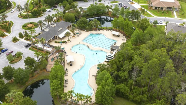 Vista aérea de un resort con una amplia piscina, rodeado de palmeras y un pequeño lago.