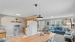 A modern kitchen with a wooden table, white cabinets, and a microwave. There is a dining area with chairs and a sofa in the background. - 8 min to Ark, Playroom, Sleeps 12 on Quiet Street (Williamstown)