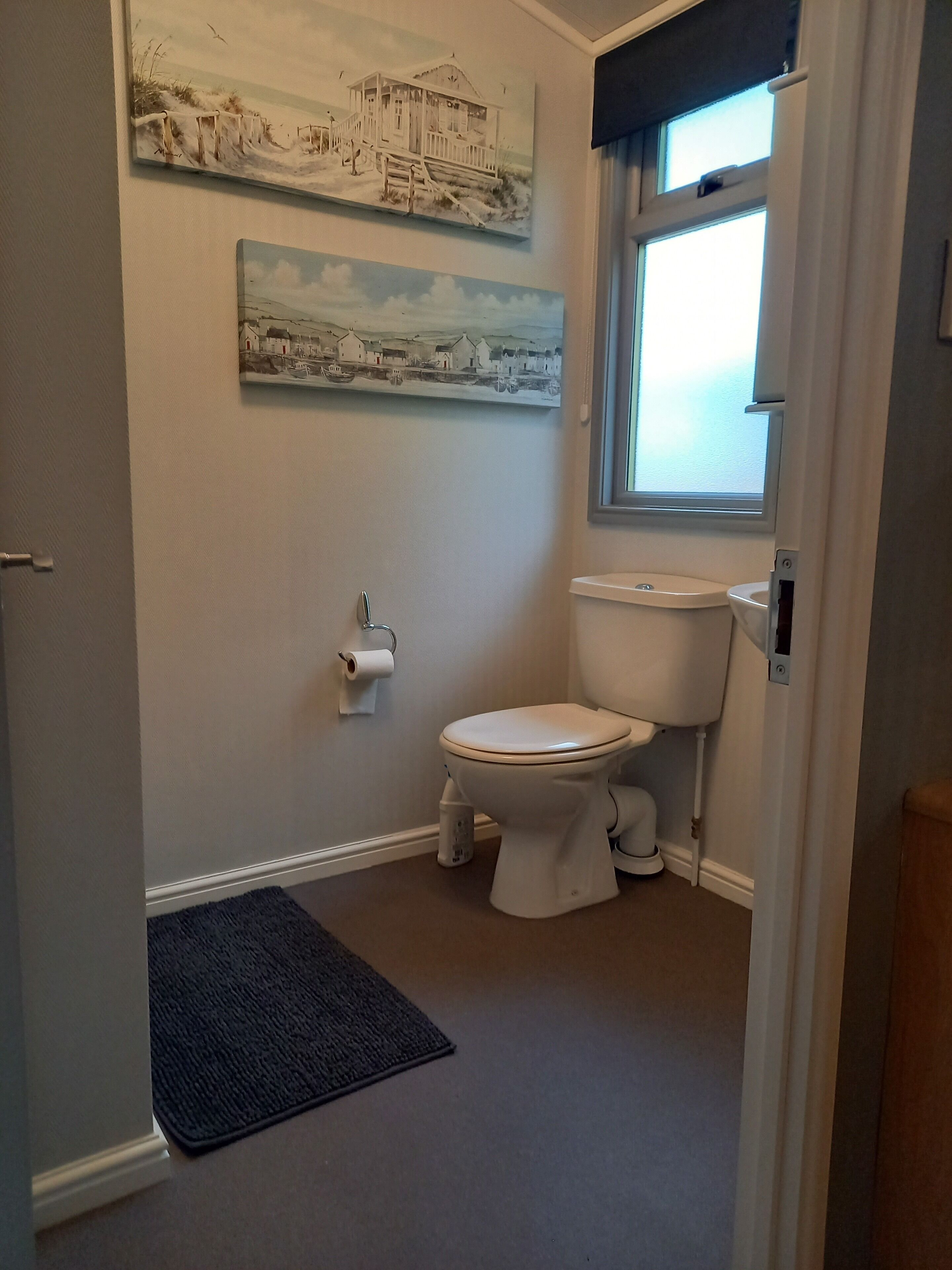 A bathroom with a toilet, a window, and two wall-mounted paintings.