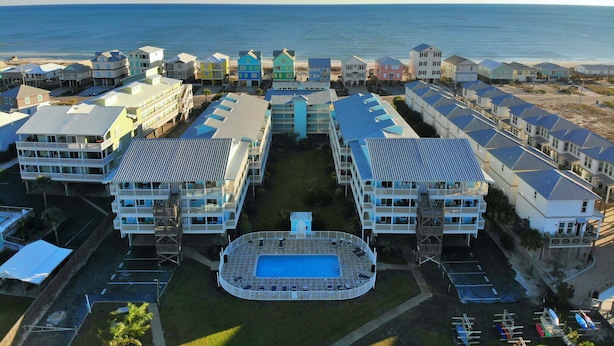 Hotel à beira-mar com vários edifícios, piscina central e vista para o oceano.