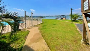 Caminho que leva a uma área de piscina, com vista para uma marina e uma ponte ao longe.
