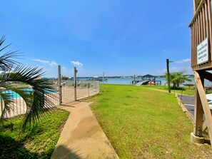 Caminho que leva a uma área de piscina, com vista para uma marina e uma ponte ao longe.
