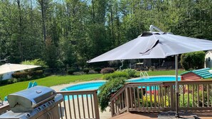 Un jardin avec une piscine, un barbecue et une terrasse couverte.