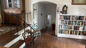 Een houten trap die leidt naar een tweede verdieping, een boekenplank vol boeken en een eetgedeelte met een houten tafel en stoelen.