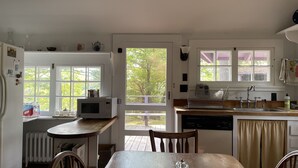 Een keuken met een raam, een magnetron, een spoelbak en een eethoek met een tafel en stoelen.