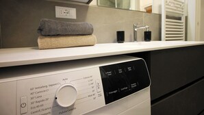 A modern bathroom with a white countertop, a mirror, and a built-in washing machine. - Casa 4 Pioppi - View and relaxation (Cavalese)