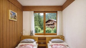 A bedroom with two beds, a window with a view of a forest and a cabin, wooden walls, and a painting on the wall. - Casa 4 Pioppi - View and relaxation (Cavalese)