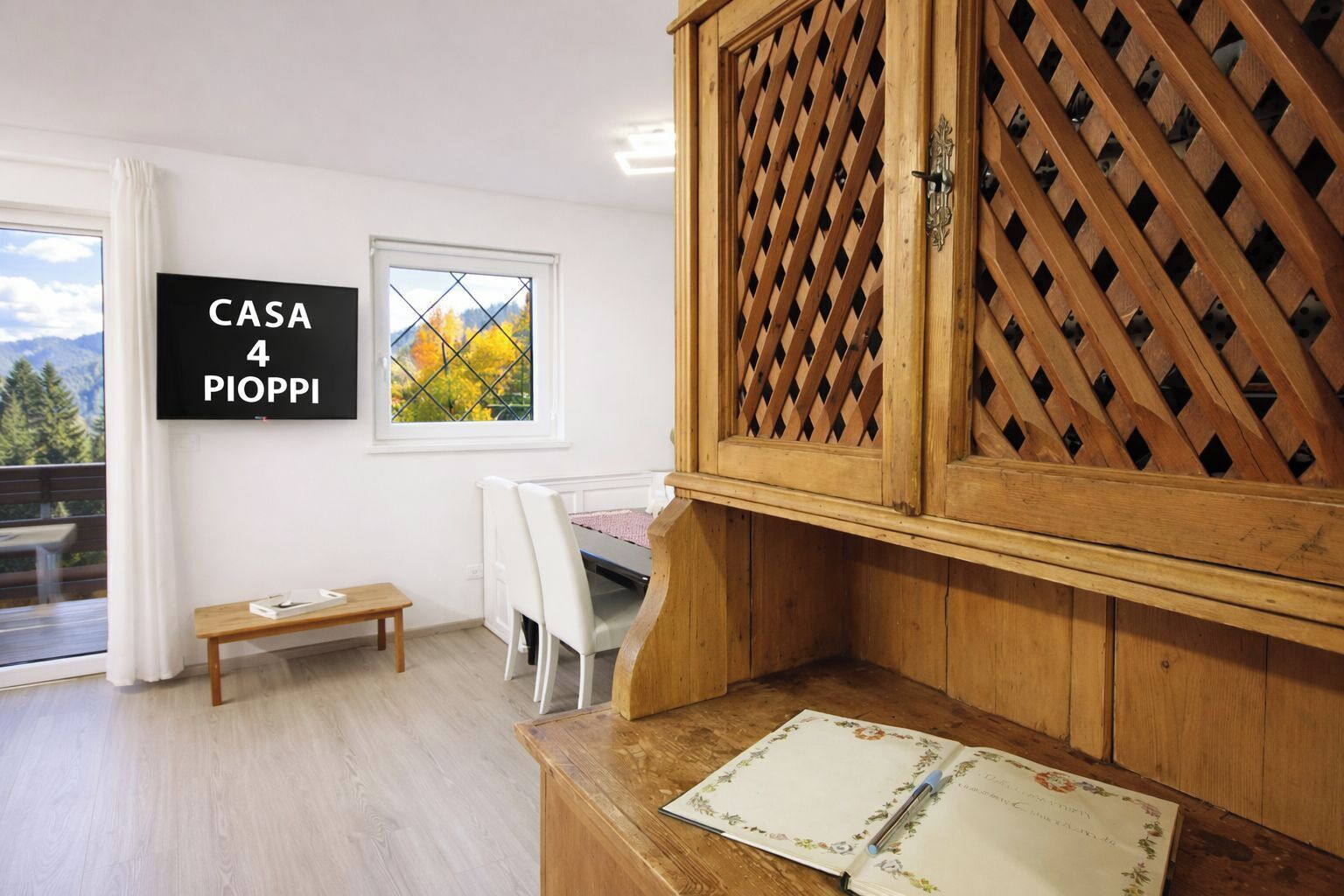 Ett rum med ett träskåp, ett litet bord, en bänk, en säng, ett fönster med utsikt över träd och en skylt med texten ”CASA 4 PIOPPI”.