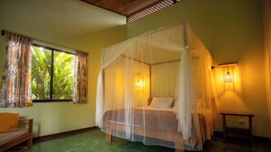 A room with a bed under a canopy, a window with curtains, a bedside table, and a small sofa.