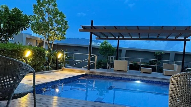 Una piscina con bordo in legno, circondata da poltrone prendisole e un pergolato.