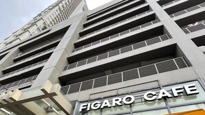 Un edificio moderno con un caffè chiamato "Figaro Cafe" dotato di posti a sedere all'aperto e ombrelloni gialli.
