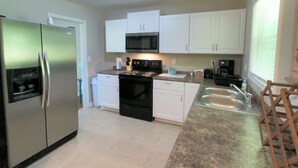 A modern kitchen with white cabinets, a stainless steel refrigerator, a microwave, a stove, and a sink.