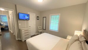 A bedroom with a bed, a dresser, a television on the wall, and a window with blinds.
